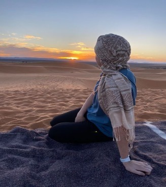 Woman sitting on blanket looking at the sunset on the Moroccan desert.